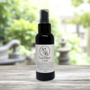 Calm Mist Sacred Blends spray bottle in a dark glass container with label, placed on a wooden surface outdoors; 100ml calming fragrance.