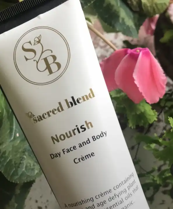 Nourish Day Face and Body Crème by Sacred Blend in a tube with floral background.