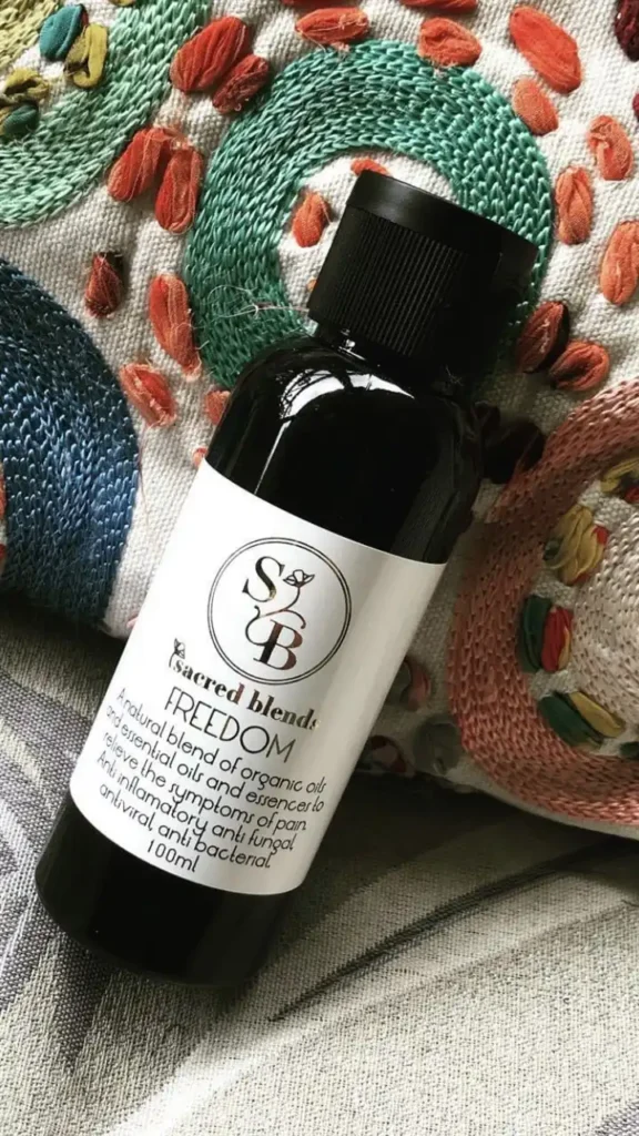 Bottle of Sacred Blend's FREEDOM organic oil displayed on a textured fabric background.