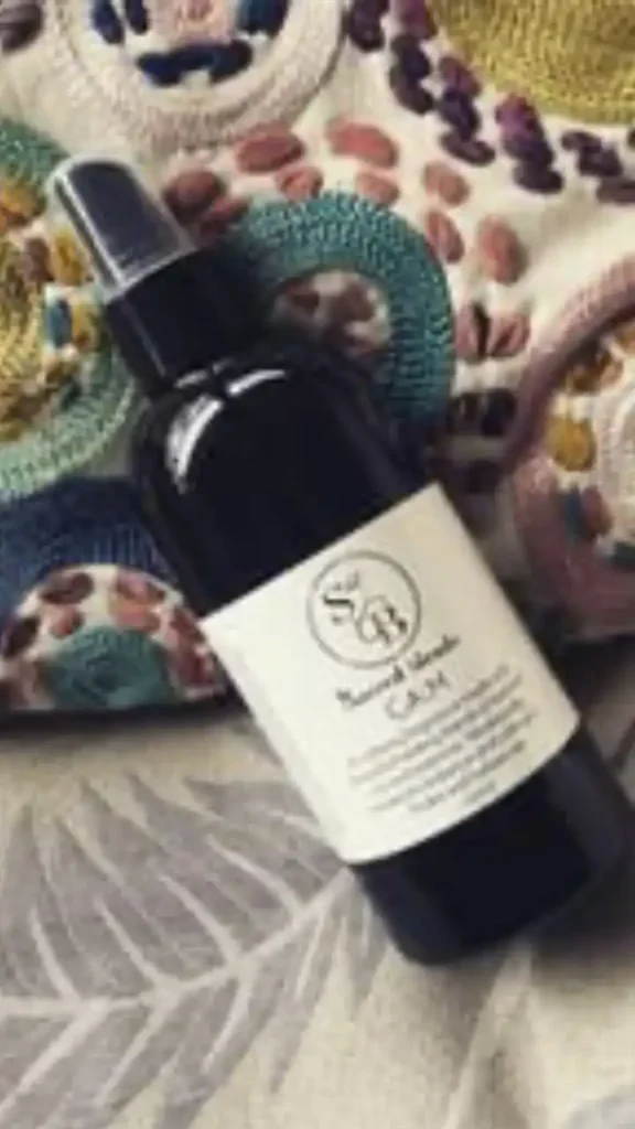 Black spray bottle labeled 'Sacred Blends Calm' placed on a textured fabric background.