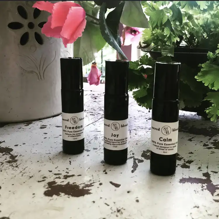 Three essential oil roll-on bottles labeled Freedom, Joy, and Calm from Sacred Blends on a textured surface.