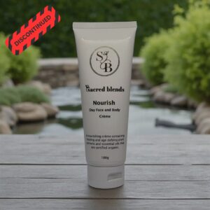A Sacred Blends Nourish Day Face and Body Crème tube stands on a wooden surface with a red discontinued label in the corner.
